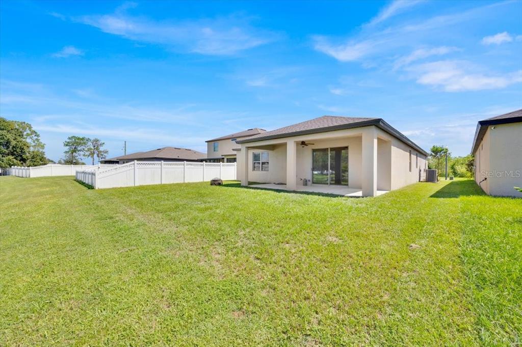 A view of a house backyard featuring a covered patio, lawn, and white vinyl fencing — 8755 RINDGE ROAD, POLK CITY, FL