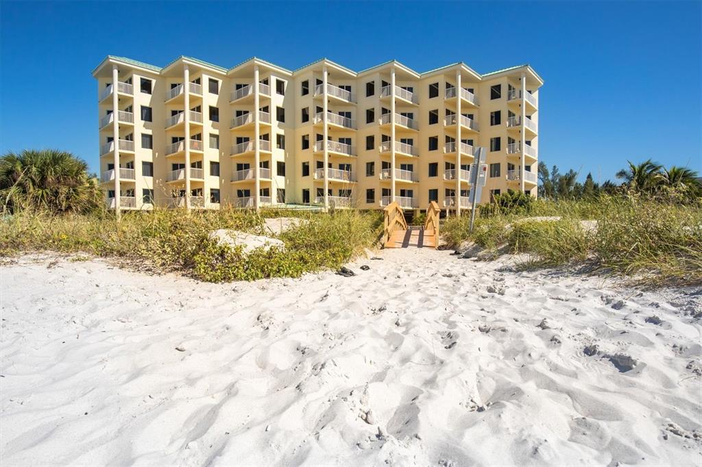 A multi-story yellow apartment building stands behind a sandy beach with a wooden walkway — 12000 GULF BOULEVARD UNIT 207N, TREASURE ISLAND, FL