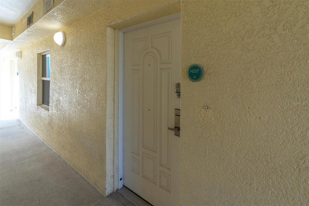 A white apartment door labeled N207 is set in a textured yellow exterior wall — 12000 GULF BOULEVARD UNIT 207N, TREASURE ISLAND, FL