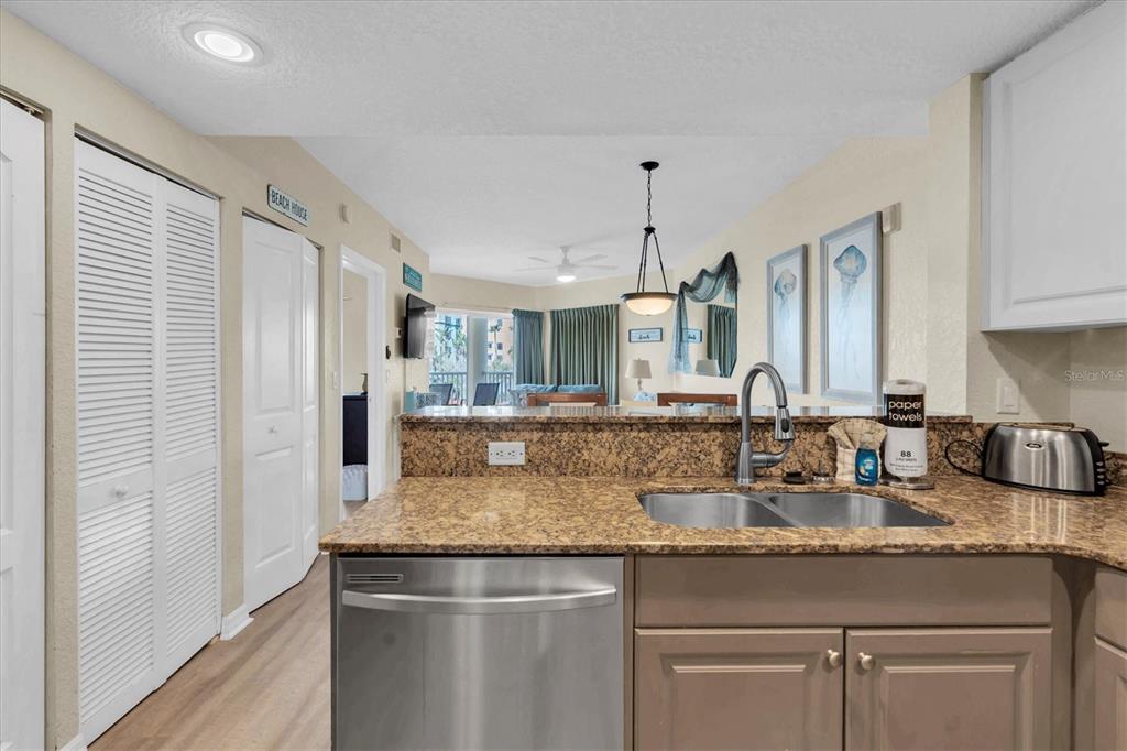 A kitchen with granite countertops and stainless steel appliances overlooks a living area — 12000 GULF BOULEVARD UNIT 207N, TREASURE ISLAND, FL