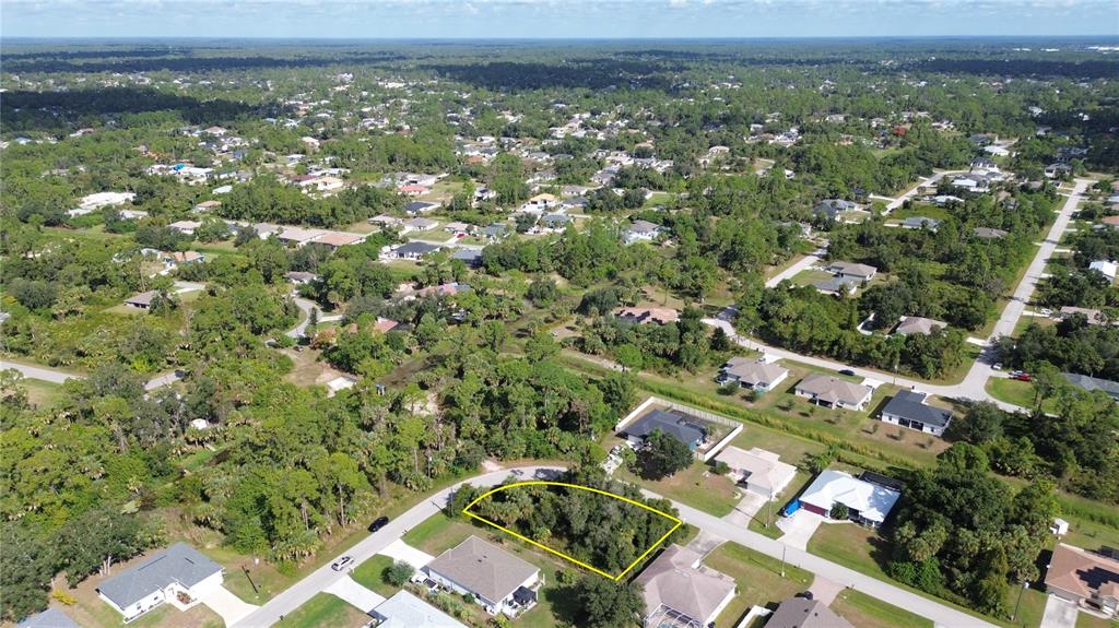 An aerial view shows a vacant, wooded residential lot outlined in yellow within a neighborhood — PETUNIA TERRACE, NORTH PORT, FL