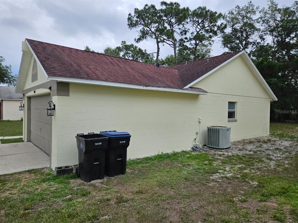 The exterior of a light yellow concrete block house with a garage and two trash cans — 9687 LINGWOOD TRAIL, ORLANDO, FL