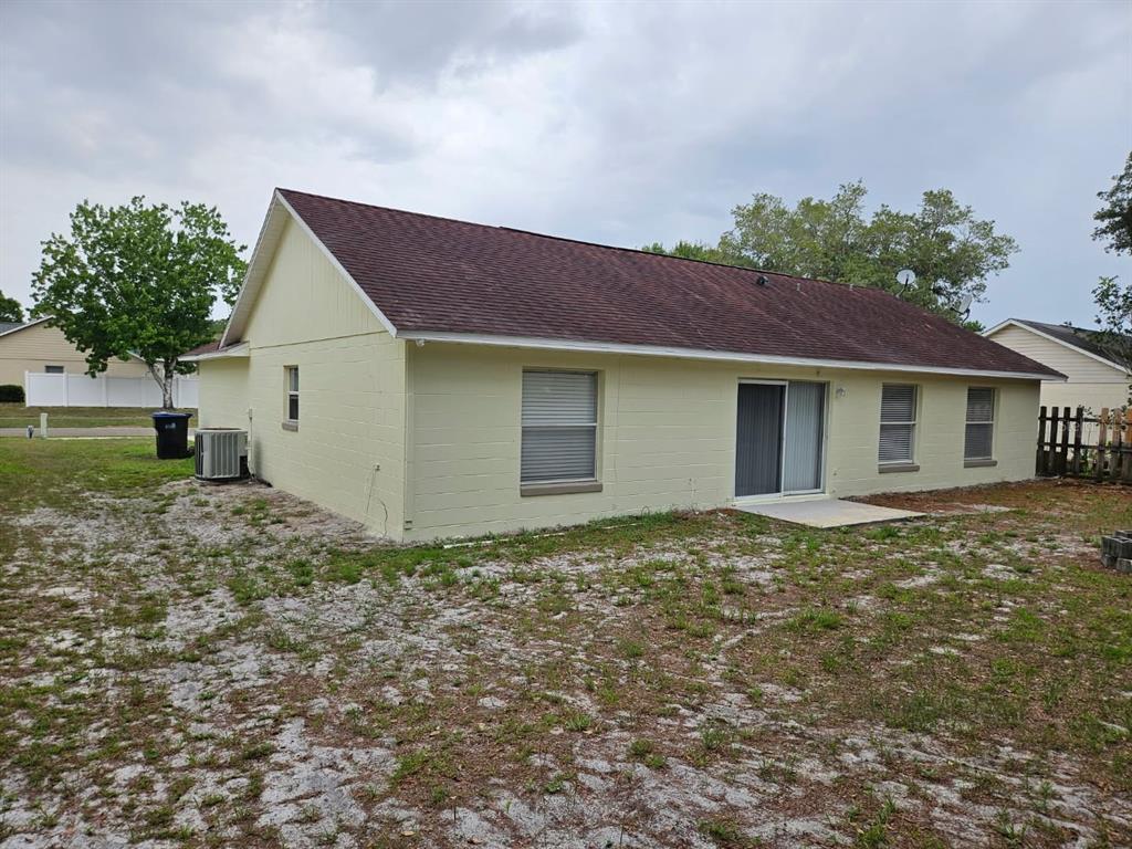 The exterior of a light yellow, single-story concrete block house with a dark shingled roof — 9687 LINGWOOD TRAIL, ORLANDO, FL