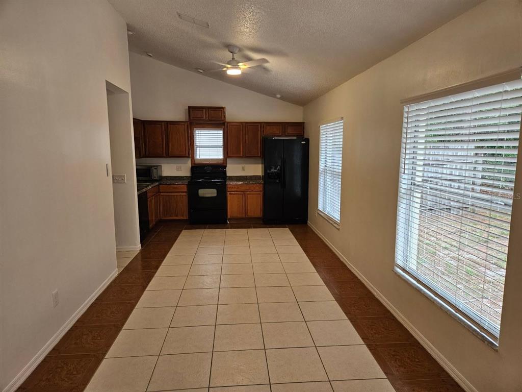 A kitchen with wood cabinets, black appliances, and a tiled floor under a vaulted ceiling — 9687 LINGWOOD TRAIL, ORLANDO, FL