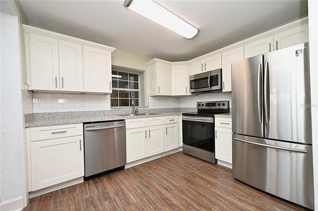 A kitchen with white cabinets, stainless steel appliances, granite countertops, and wood-look flooring — 3958 2ND STREET NW, LAKELAND, FL
