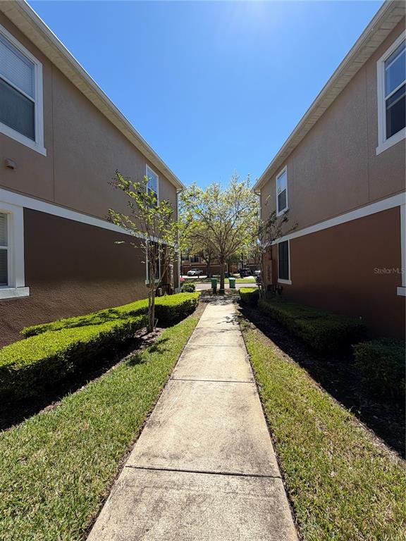 A concrete walkway leads between two multi-story residential buildings with manicured hedges and trees — 15353 OAK APPLE COURT, WINTER GARDEN, FL