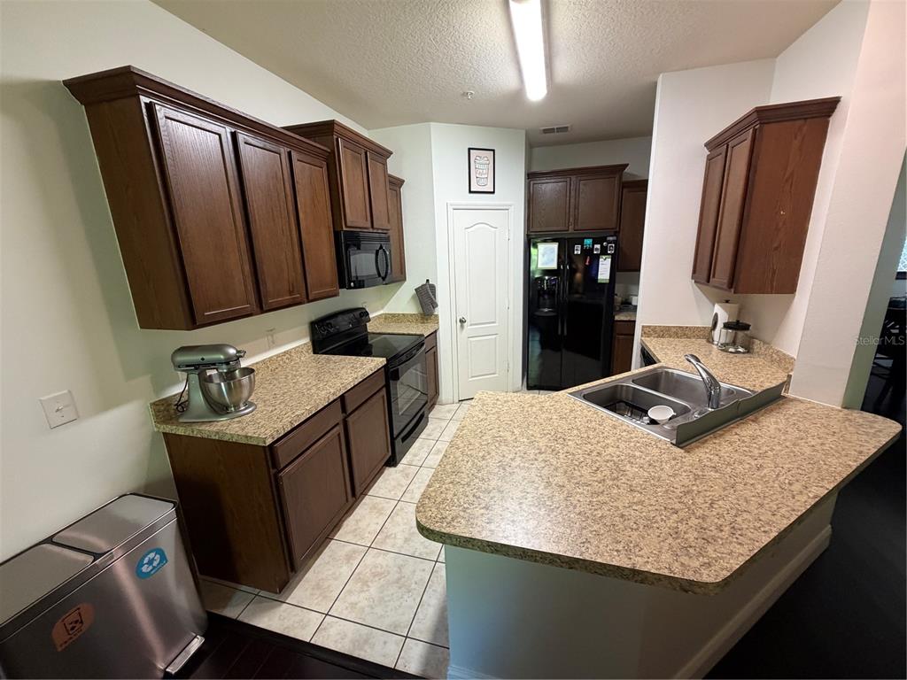 A kitchen features dark wood cabinets, speckled laminate countertops, black appliances, and tile flooring — 15353 OAK APPLE COURT, WINTER GARDEN, FL