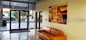 A lobby features a tan leather sofa, a large abstract wall painting, and glass entry doors — 701 S MADISON AVENUE UNIT 215, CLEARWATER, FL