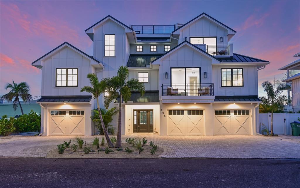 A three-story white farmhouse-style home with a three-car garage and a rooftop deck at dusk — 305 55TH STREET, HOLMES BEACH, FL