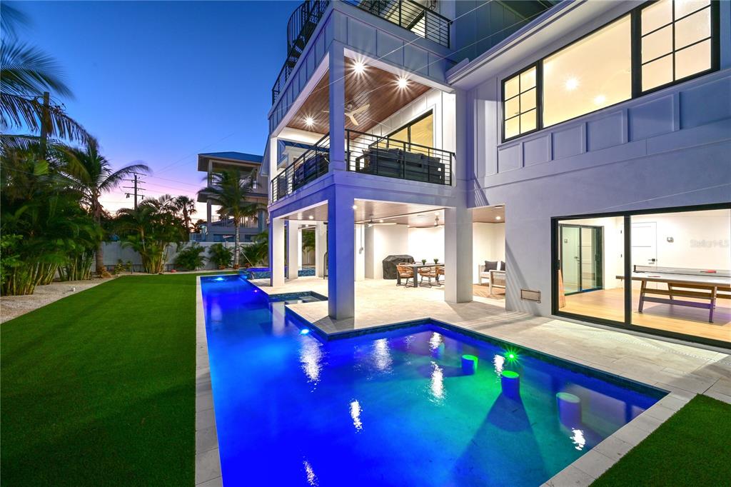 A multi-story house with a swimming pool, covered patio, and artificial turf lawn at dusk — 305 55TH STREET, HOLMES BEACH, FL