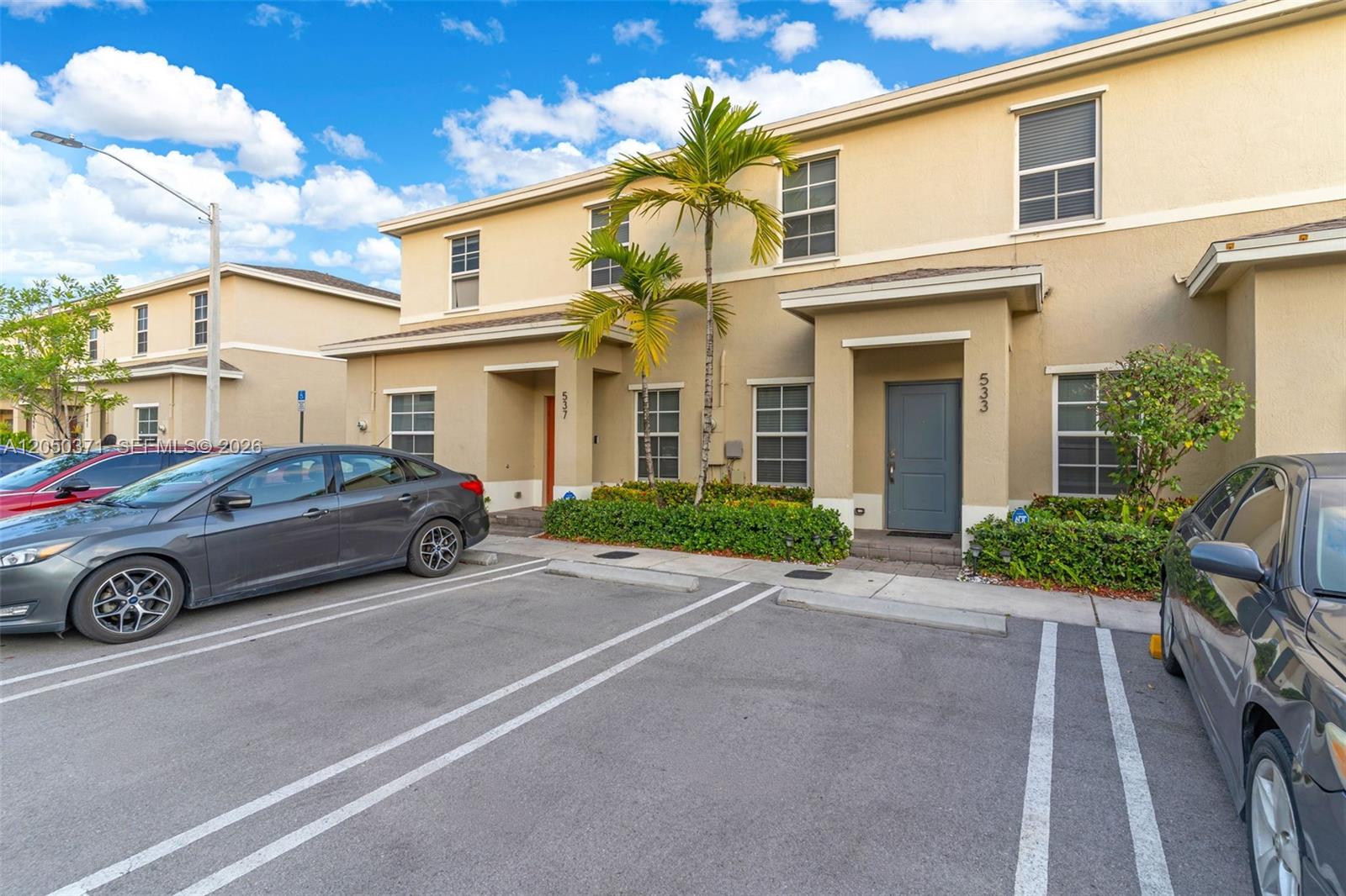 Two-story townhouses with beige stucco exteriors and assigned parking spaces in front — 533 NE 5th Pl, Florida City FL 33034, FLORIDA CITY, FL