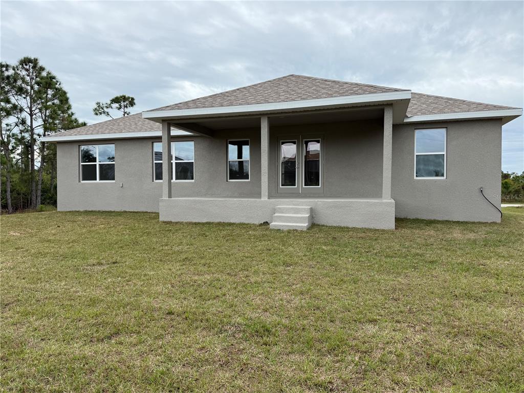The rear exterior of a single-story house features a covered patio and a grassy yard — 14184 SALVATIERRA LANE, PORT CHARLOTTE, FL