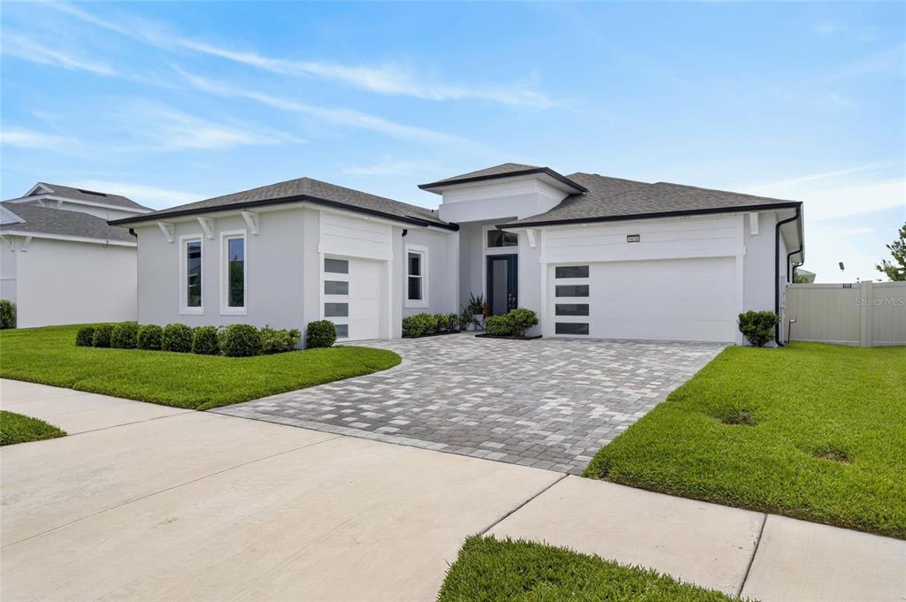 A modern single-story house with a paver driveway, white stucco exterior, and a three-car garage — 8634 DRUMMER PLANK DRIVE, WESLEY CHAPEL, FL