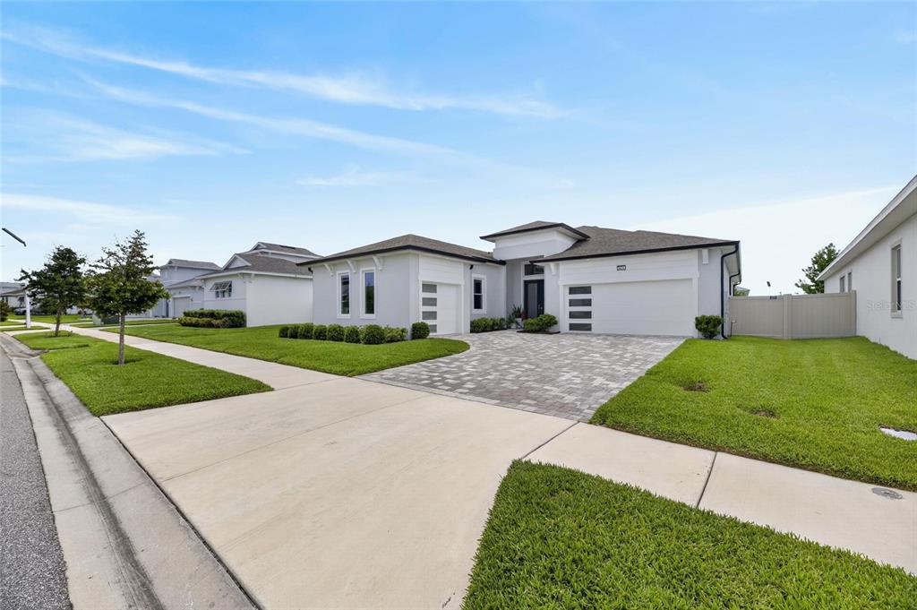 A modern, single-story suburban house with a white exterior, paver driveway, and attached garage — 8634 DRUMMER PLANK DRIVE, WESLEY CHAPEL, FL