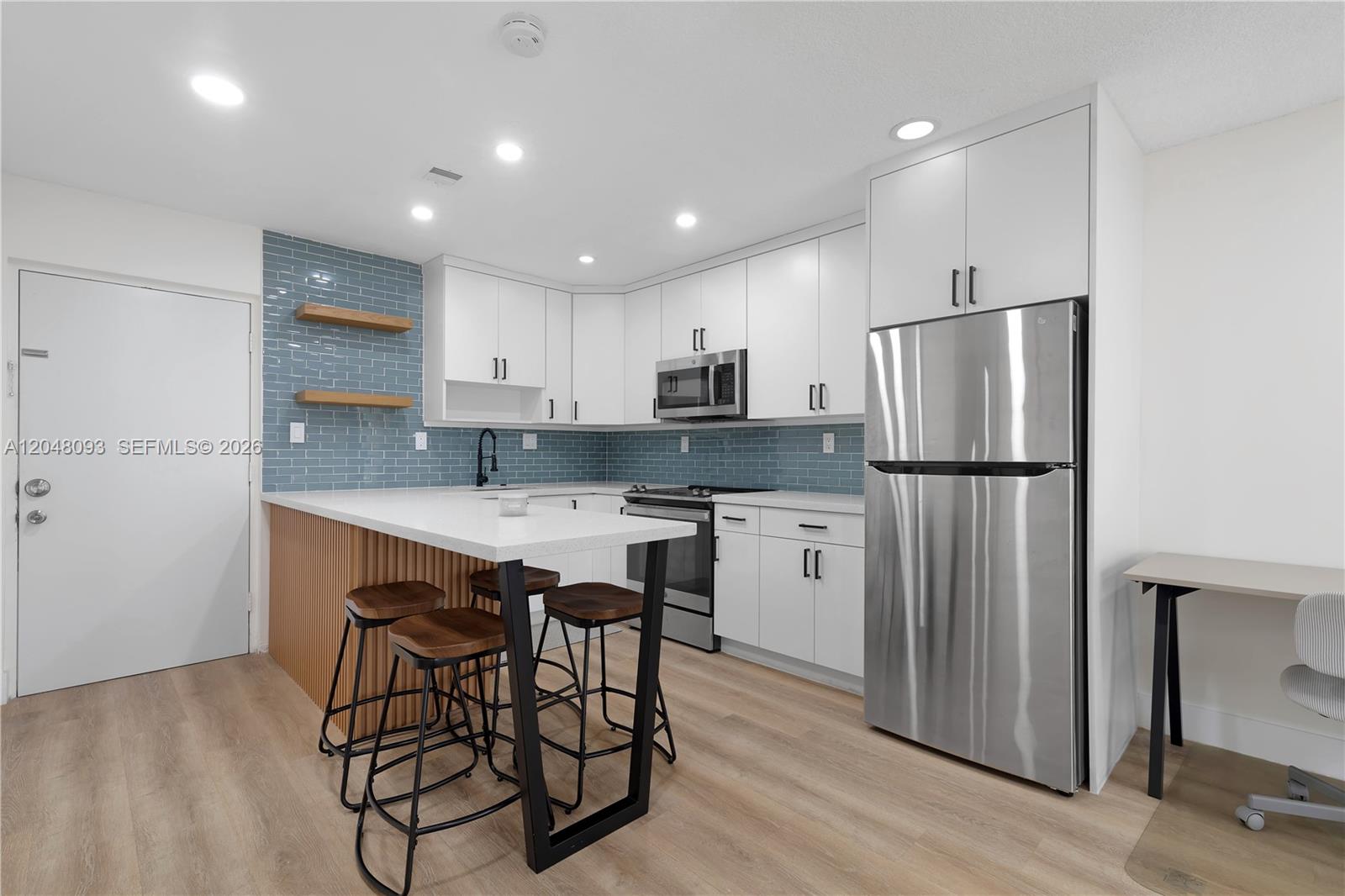A modern kitchen features white cabinets, a blue tiled backsplash, and a wooden breakfast bar — 9520 SW 8th St # 203, Miami FL 33174, MIAMI, FL