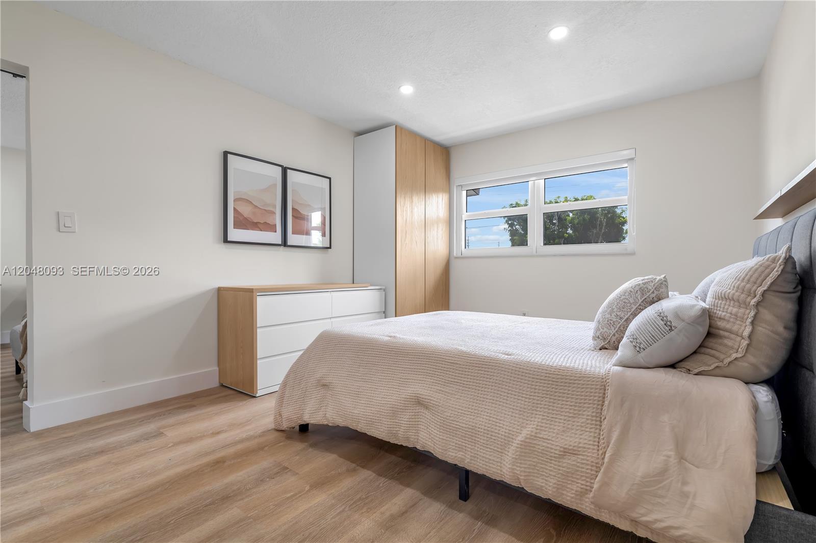 A bedroom features light wood flooring, a bed with beige bedding, and a white dresser — 9520 SW 8th St # 203, Miami FL 33174, MIAMI, FL