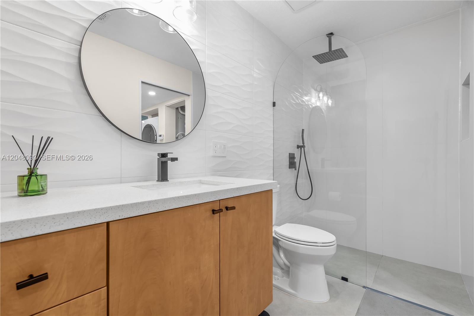 A modern bathroom features a wood vanity, round mirror, and a glass-enclosed walk-in shower — 9520 SW 8th St # 203, Miami FL 33174, MIAMI, FL