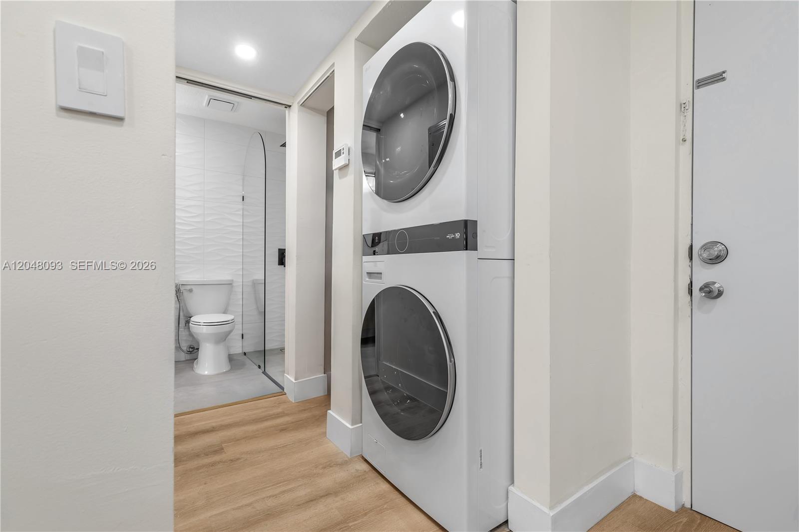 A stacked washer and dryer unit stands in a hallway next to a bathroom — 9520 SW 8th St # 203, Miami FL 33174, MIAMI, FL