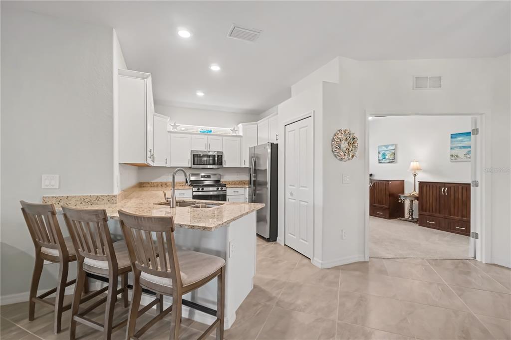 A kitchen with white cabinets, granite countertops, and a breakfast bar with three wooden chairs — 17848 PALMETTO PASS LANE, PUNTA GORDA, FL