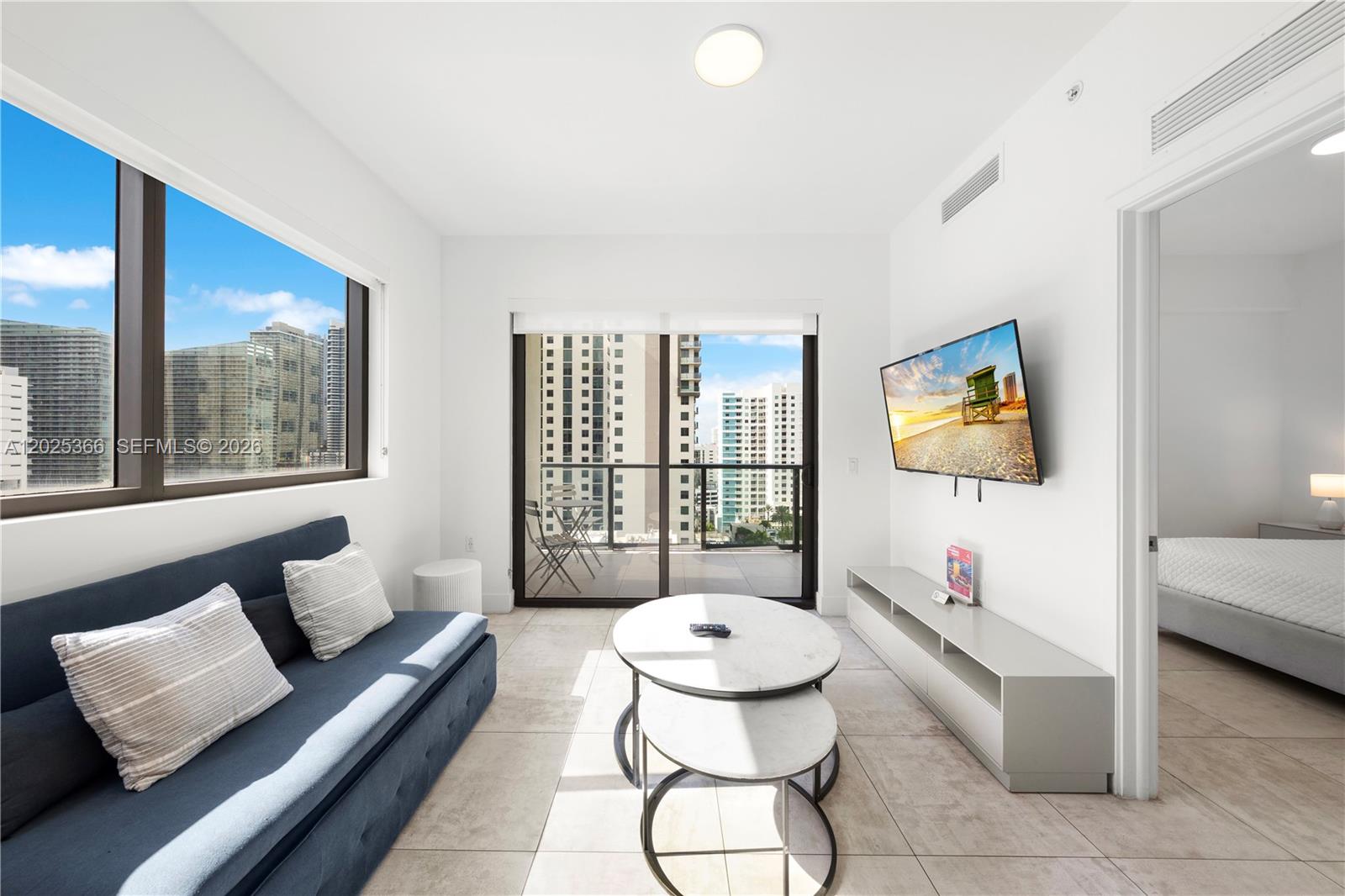 A living room features a blue sofa, nested coffee tables, a wall-mounted television, and a balcony — 239 SW 9th St # 1701, Miami FL 33130, MIAMI, FL