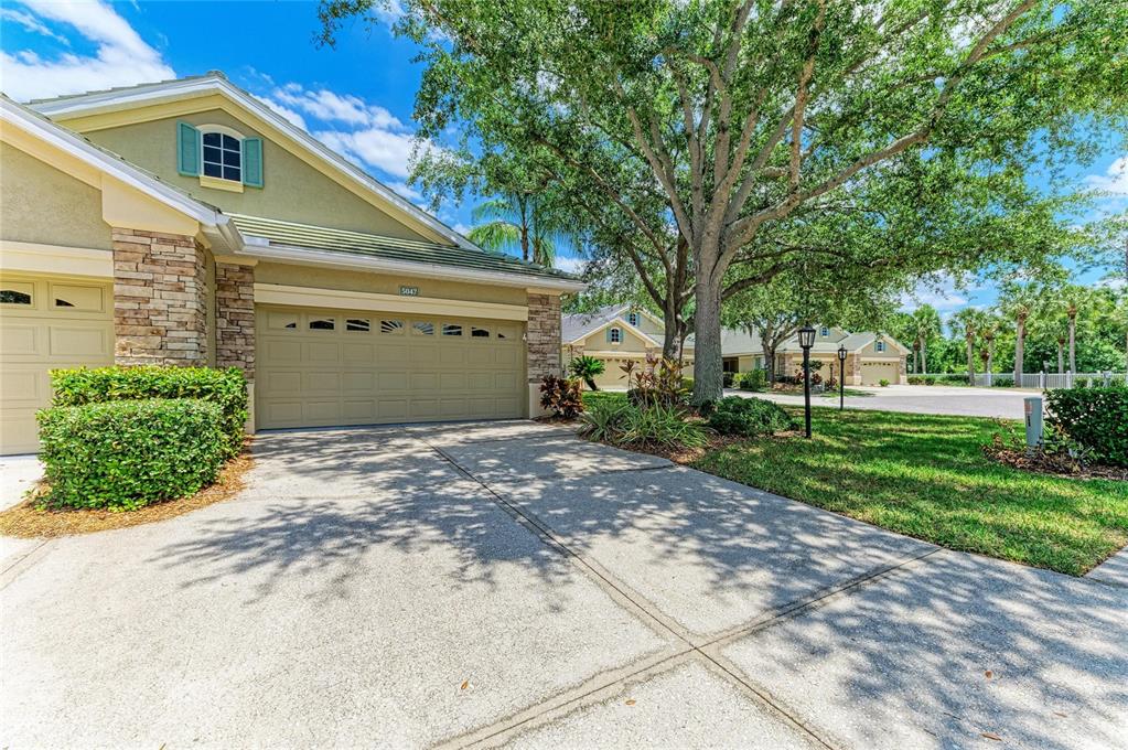 A tan house with a stone facade, a two-car garage, and a large shade tree — 5047 LAKESCENE PLACE, SARASOTA, FL