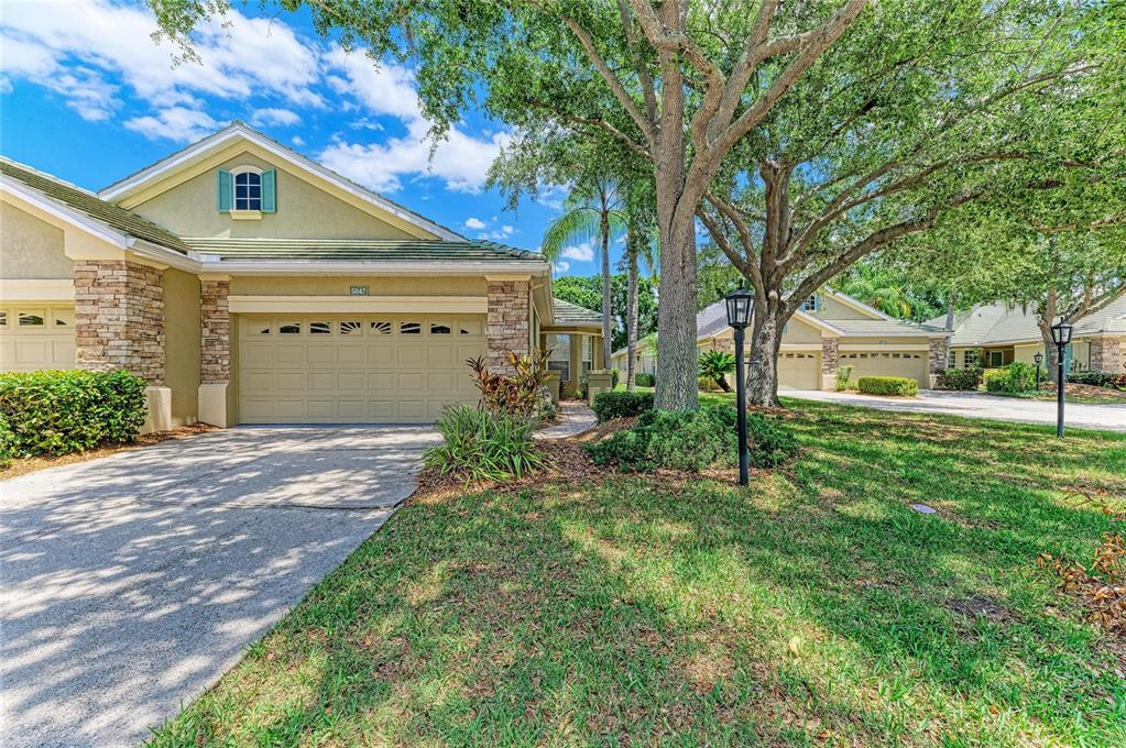 A tan house with a stone-accented garage and a large tree in the front yard — 5047 LAKESCENE PLACE, SARASOTA, FL