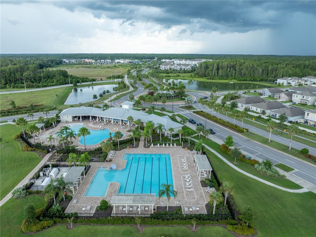 An aerial view shows a community swimming pool complex with a clubhouse and surrounding landscaping — 2886 SUNCOAST PLAINS DRIVE, ODESSA, FL