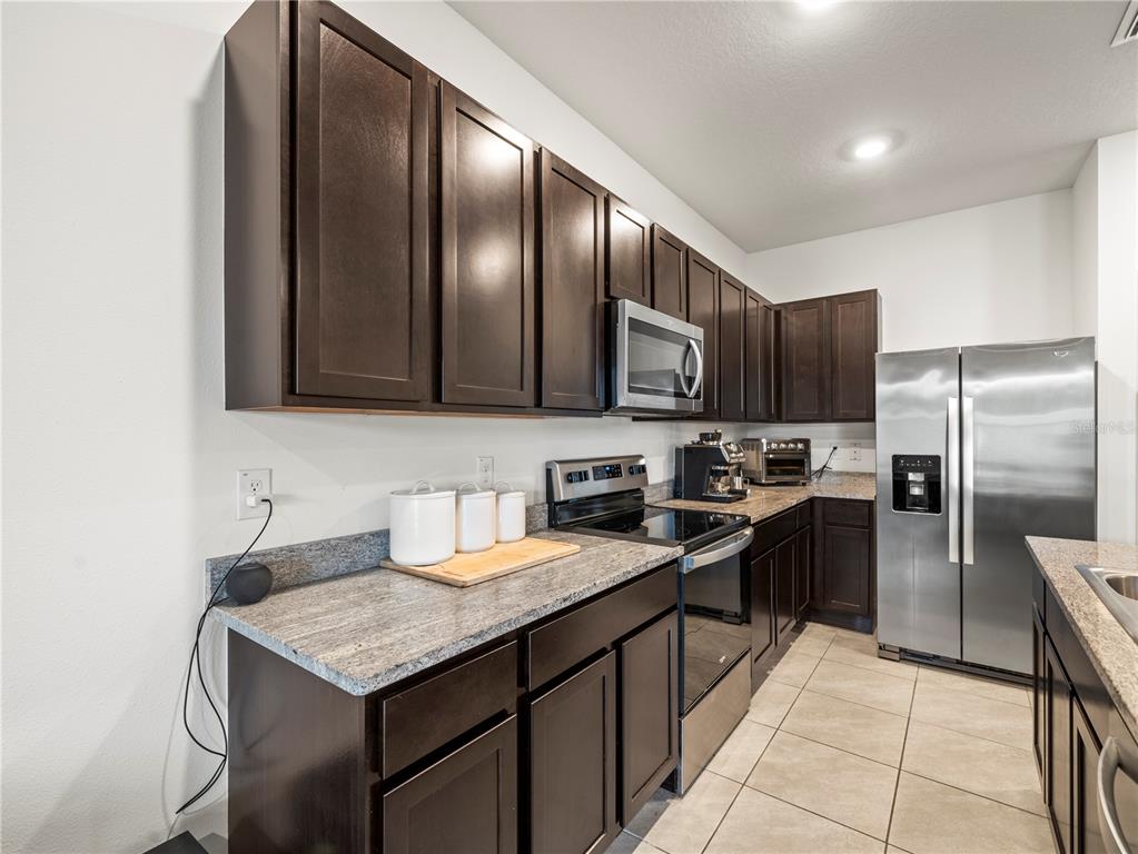 A kitchen features dark wood cabinets, granite countertops, and stainless steel appliances — 2886 SUNCOAST PLAINS DRIVE, ODESSA, FL