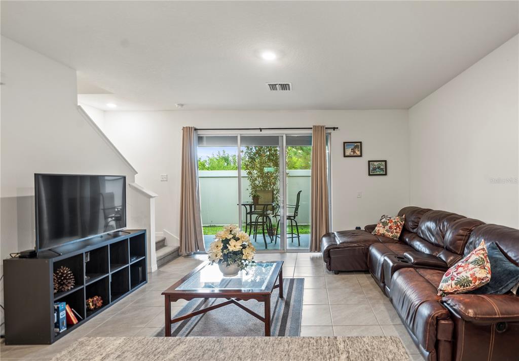 A living room features tile flooring, a brown leather sectional, a television stand, and sliding doors — 2886 SUNCOAST PLAINS DRIVE, ODESSA, FL
