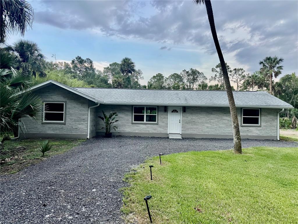 A single-story house with gray siding, a white front door, and a gravel driveway — 6381 CHERRY LANE, BUNNELL, FL