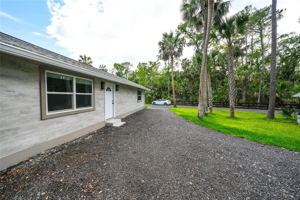 A gravel driveway leads to the side entrance of a light-colored house with palm trees — 6381 CHERRY LANE, BUNNELL, FL