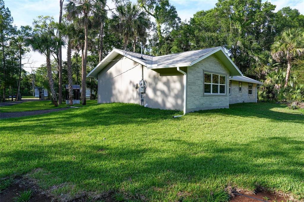 A side view of a single-story house with a light-colored stone facade and green lawn — 6381 CHERRY LANE, BUNNELL, FL
