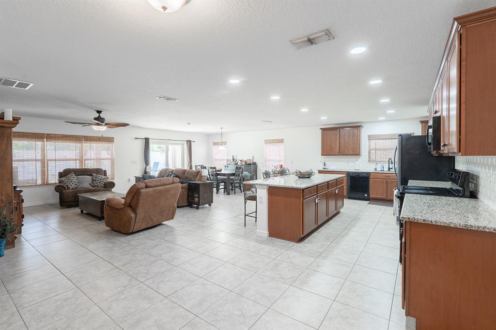 An open-concept kitchen and living area features tile flooring, wood cabinetry, and granite countertops — 11331 BRIGHTON KNOLL LOOP, RIVERVIEW, FL