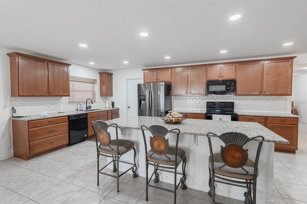 A kitchen with wood cabinets, granite countertops, a center island with stools, and tile flooring — 11331 BRIGHTON KNOLL LOOP, RIVERVIEW, FL