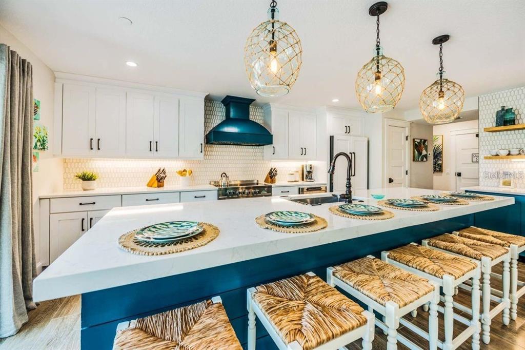 A kitchen features white cabinets, a blue island with woven stools, and three pendant lights — 332 AVENIDA DE MAYO, SARASOTA, FL