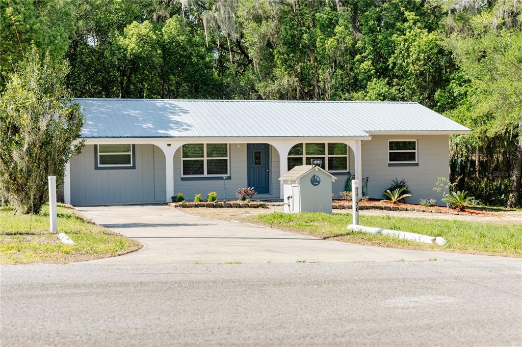 A single-story house with a metal roof, gray siding, and a concrete driveway — 24270 SW SHOREWOOD DRIVE N, DUNNELLON, FL