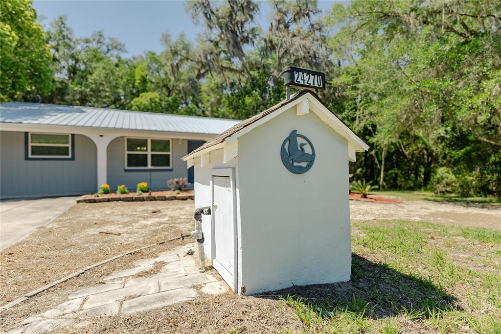 A small white utility shed with a house number sign stands in a grassy yard — 24270 SW SHOREWOOD DRIVE N, DUNNELLON, FL