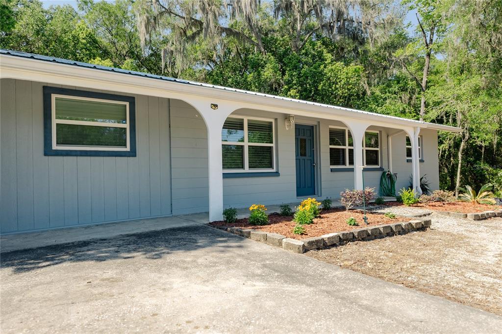 A single-story house with gray siding, a white porch, and a blue front door — 24270 SW SHOREWOOD DRIVE N, DUNNELLON, FL