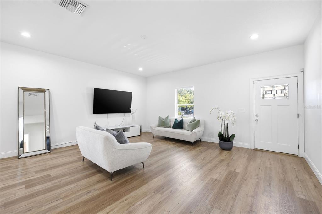 A bright living room features white walls, light wood-look flooring, a television, and two sofas — 524 S GROSSE AVE AVENUE, TARPON SPRINGS, FL