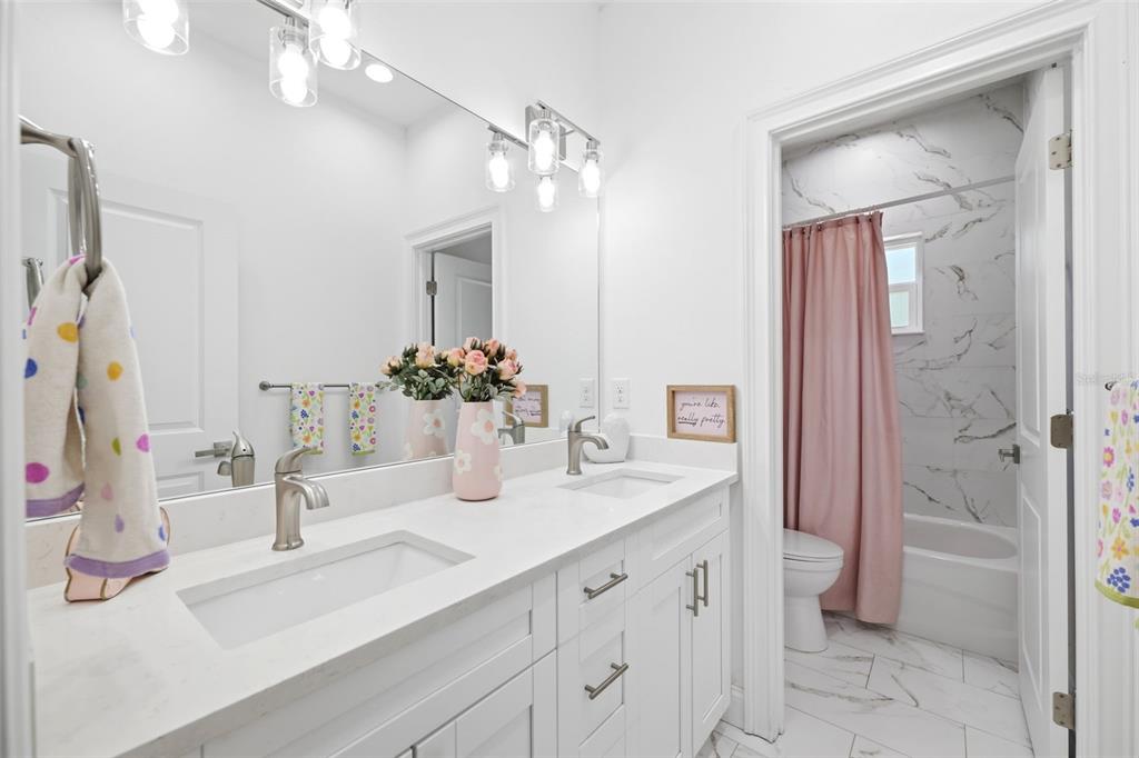 A bathroom with a double vanity, white cabinets, marble-look countertops, and a pink shower curtain — 524 S GROSSE AVE AVENUE, TARPON SPRINGS, FL