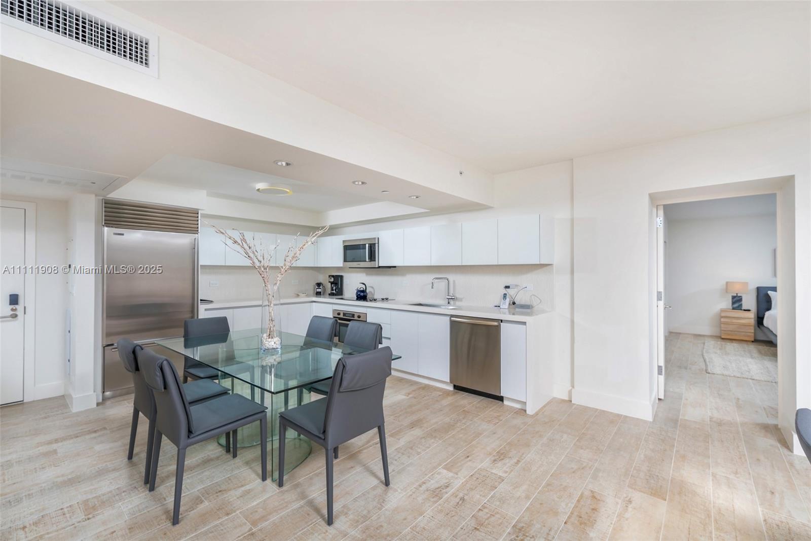 A modern kitchen features white cabinetry, stainless steel appliances, and a glass dining table — 102 24th St # 1019, Miami Beach FL 33139, MIAMI BEACH, FL