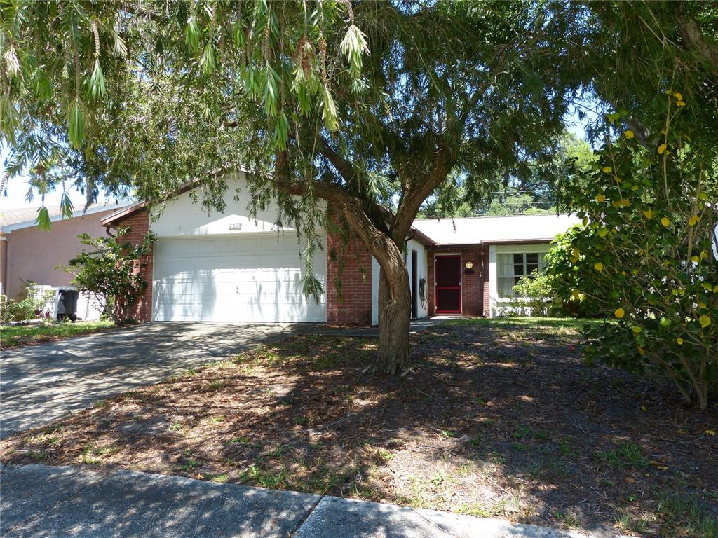 A single-story brick and white house with a two-car garage and a large front tree — 2528 ELDERBERRY DRIVE, CLEARWATER, FL