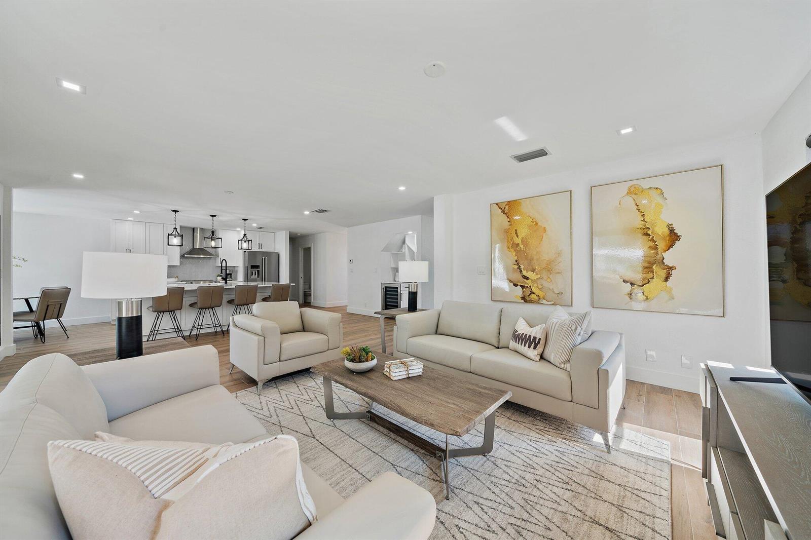 A modern living room with light-colored sofas, a wooden coffee table, and an open kitchen — 1878 Lynton Circle, Wellington FL 33414, WELLINGTON, FL