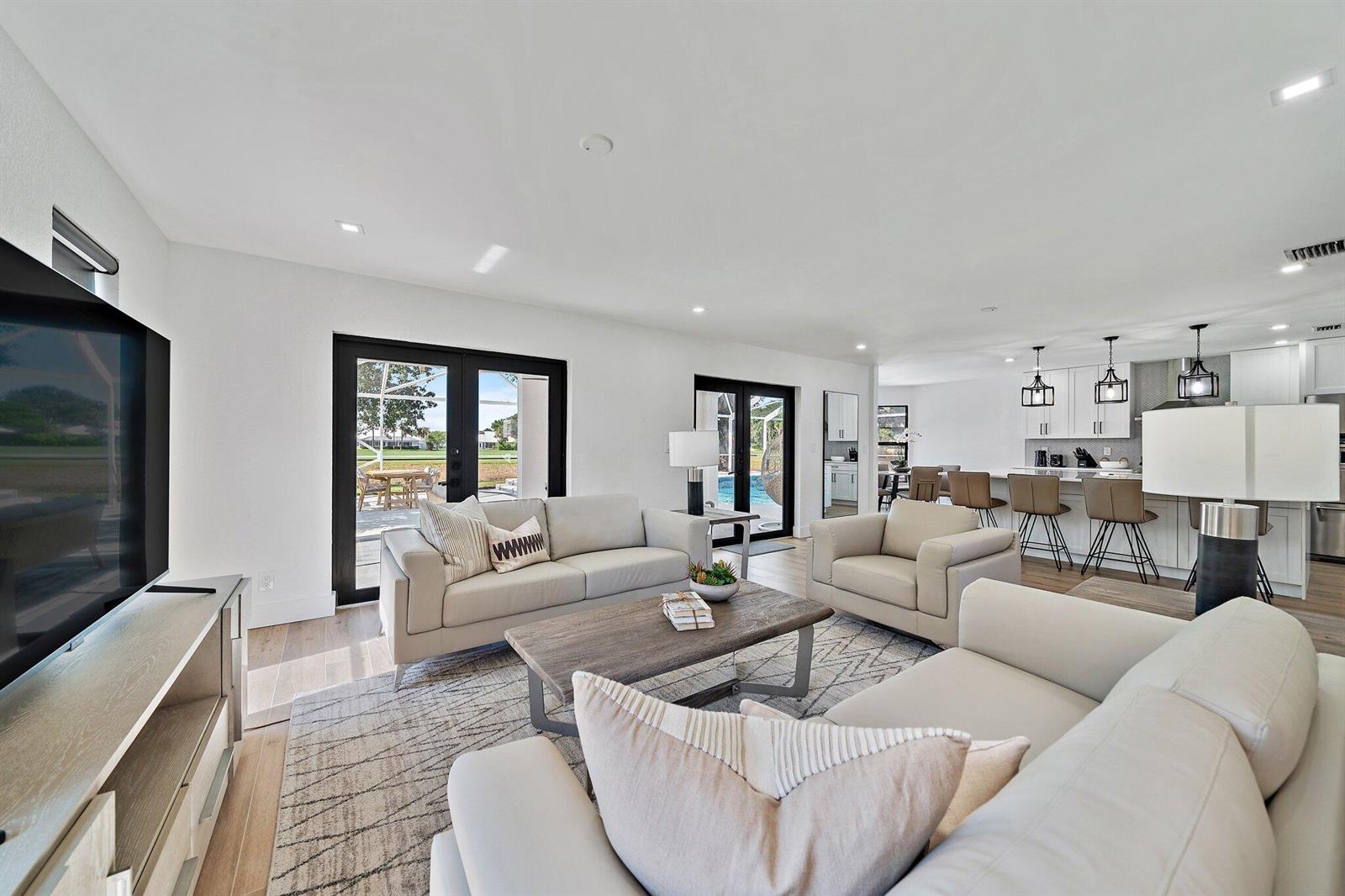 An open-concept living room and kitchen featuring light-colored furniture, hardwood floors, and glass patio doors — 1878 Lynton Circle, Wellington FL 33414, WELLINGTON, FL