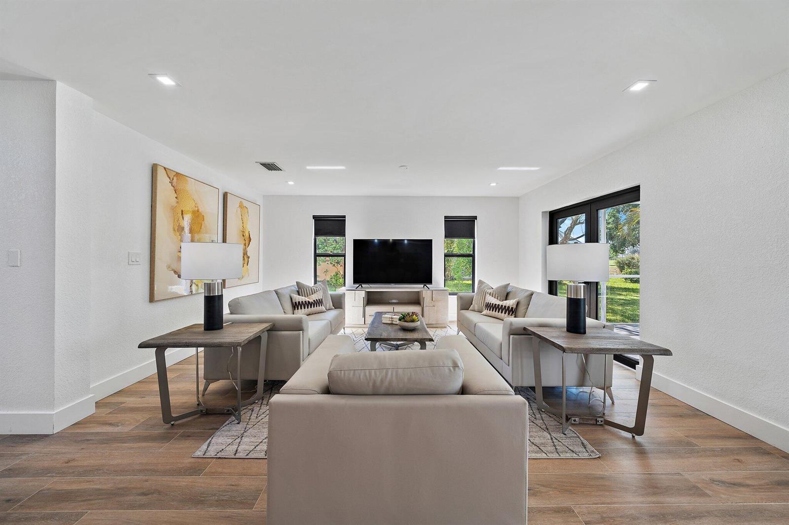 A living room features three light-colored sofas, a television, and wood-look tile flooring — 1878 Lynton Circle, Wellington FL 33414, WELLINGTON, FL