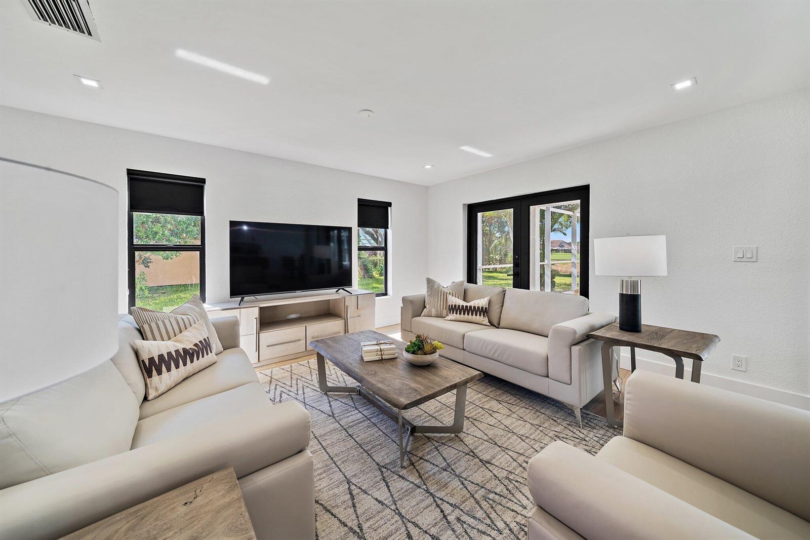 A living room features light-colored sofas, a wooden coffee table, and a television on a console — 1878 Lynton Circle, Wellington FL 33414, WELLINGTON, FL