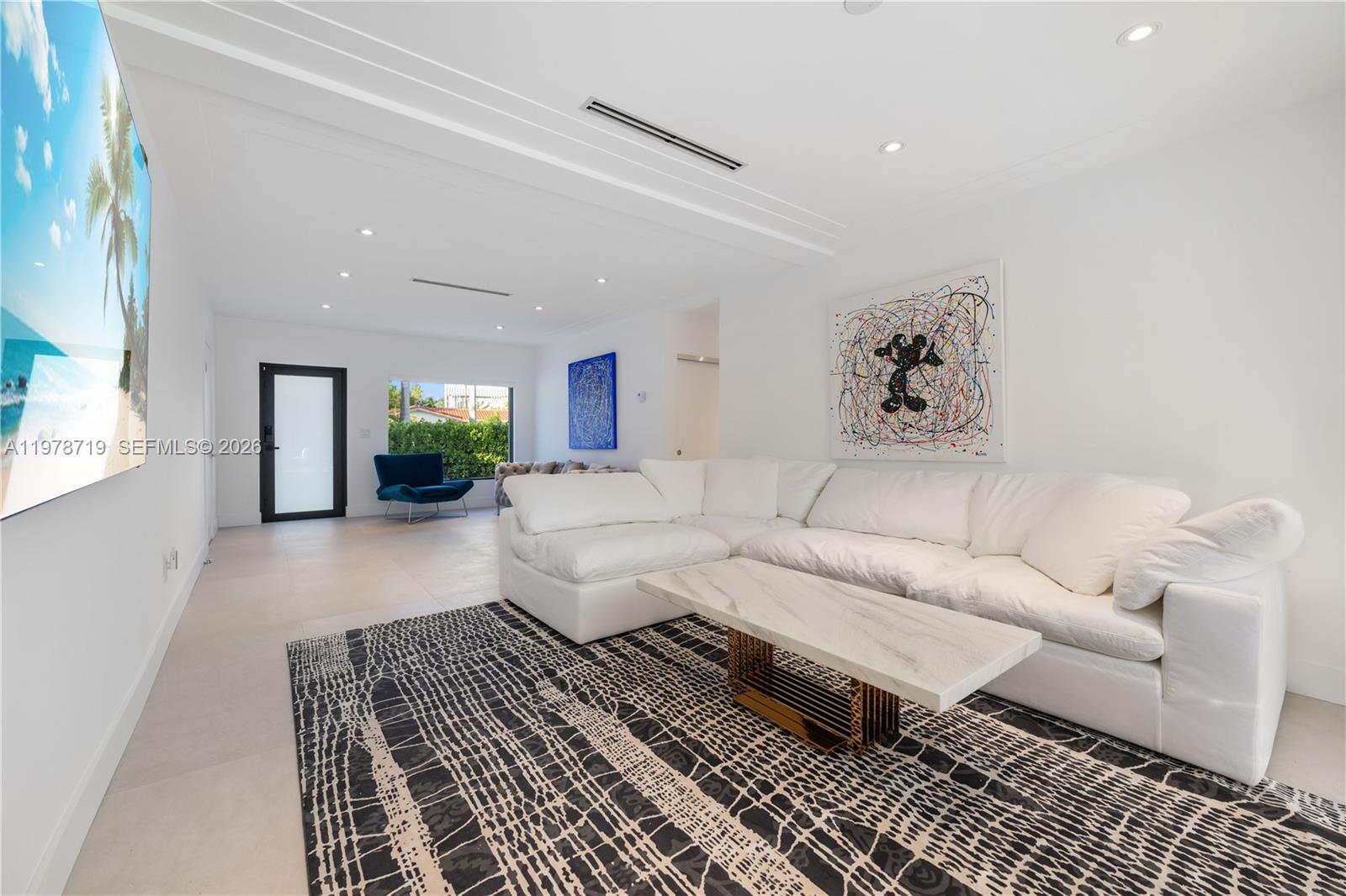 A modern living room features a white sectional sofa, a patterned rug, and abstract art — 900 W 47th Ct, Miami Beach FL 33140, MIAMI BEACH, FL