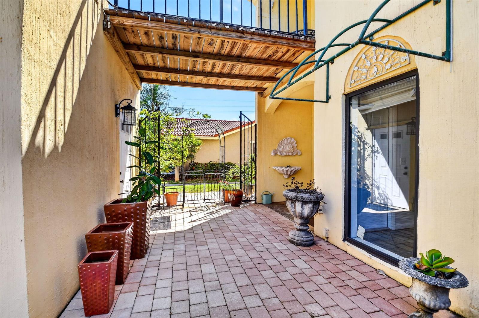 A paved outdoor patio area features potted plants, a wall fountain, and a wooden pergola — WELLINGTON, FL