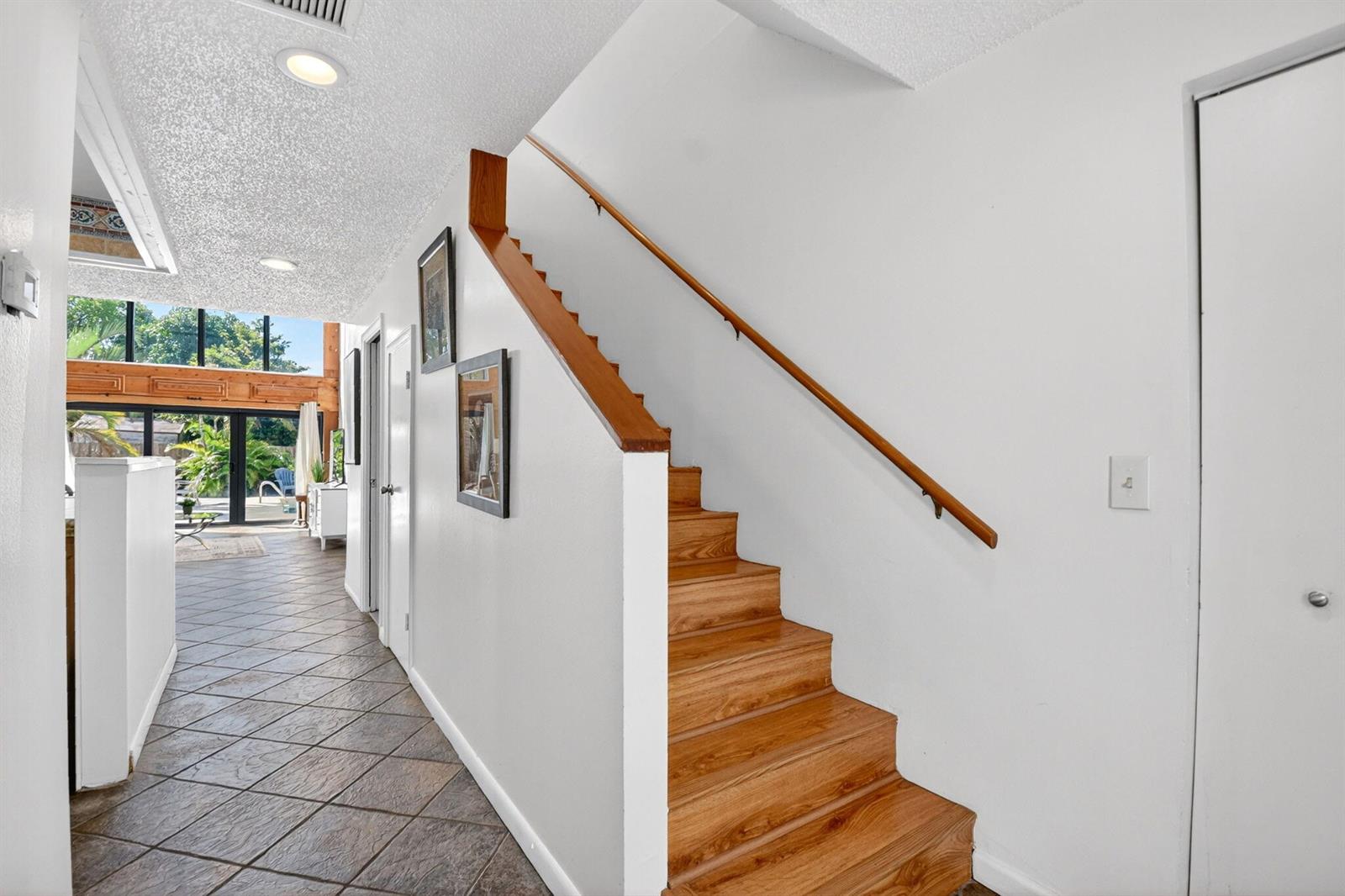 A wooden staircase with a handrail sits beside a tiled hallway leading to a patio — WELLINGTON, FL
