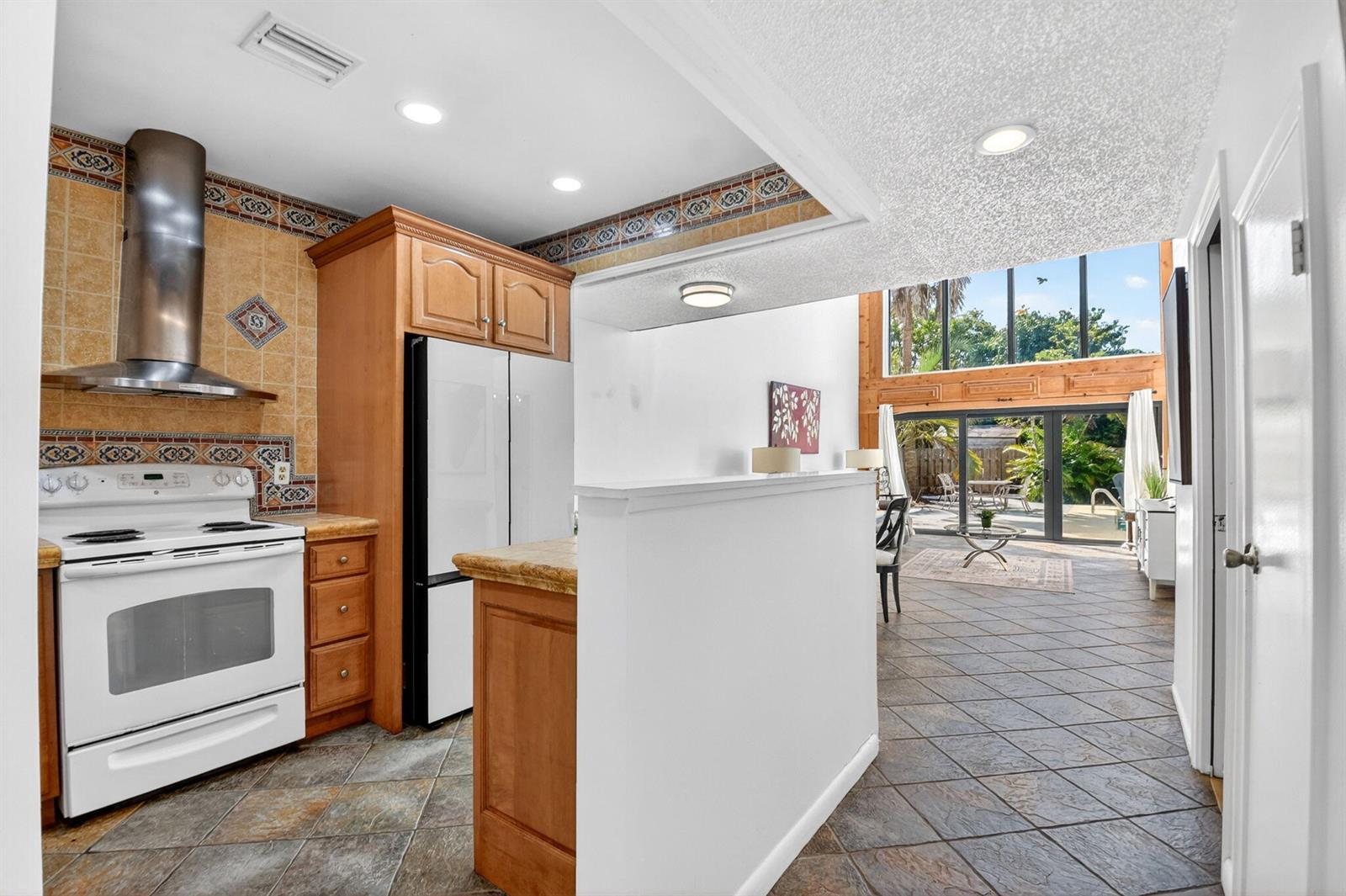 A kitchen with wood cabinets and tile backsplash opens to a living area with windows — WELLINGTON, FL